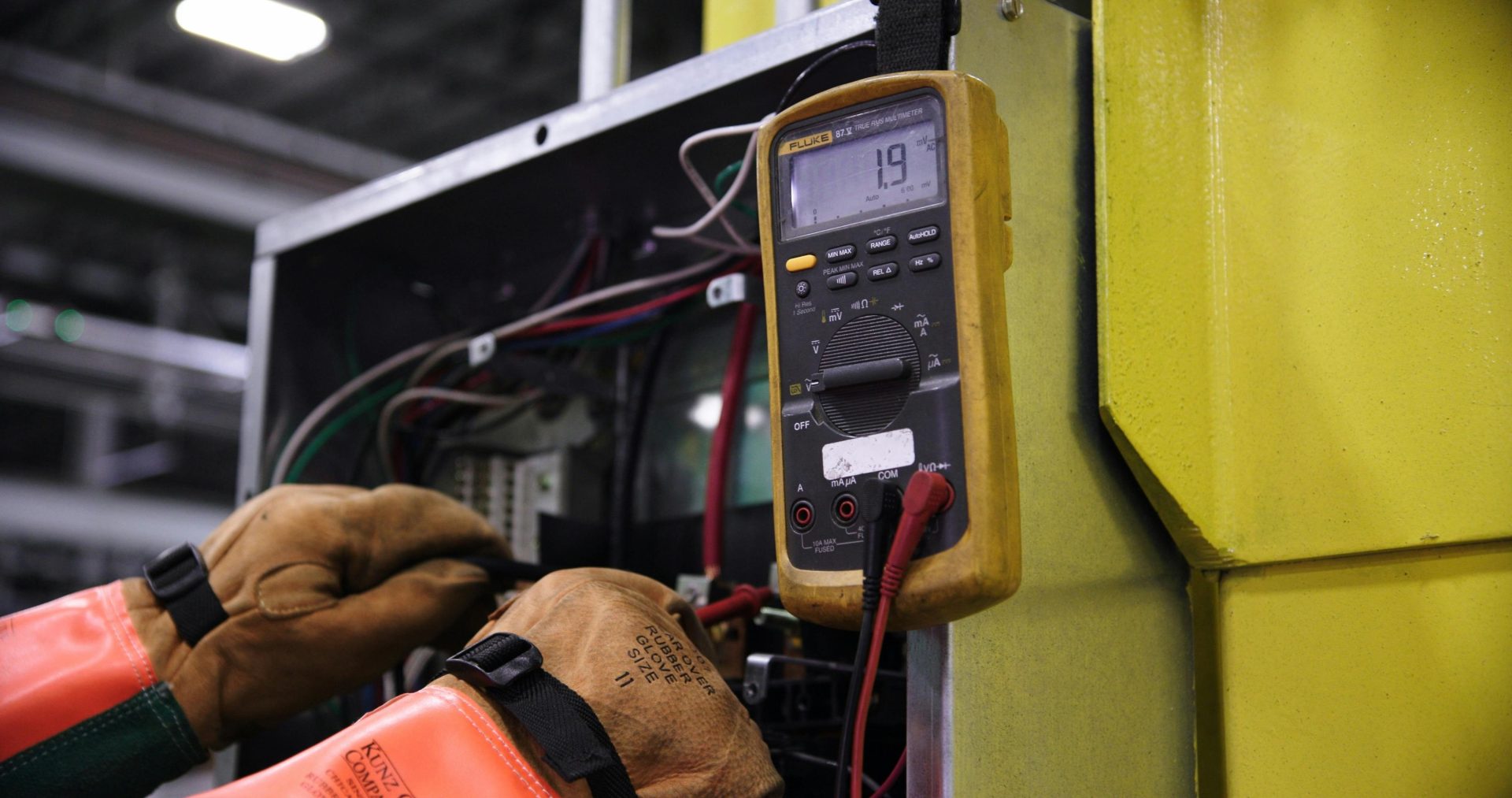 Electricista utilizando un multímetro para reparar el cableado de un panel de control industrial.