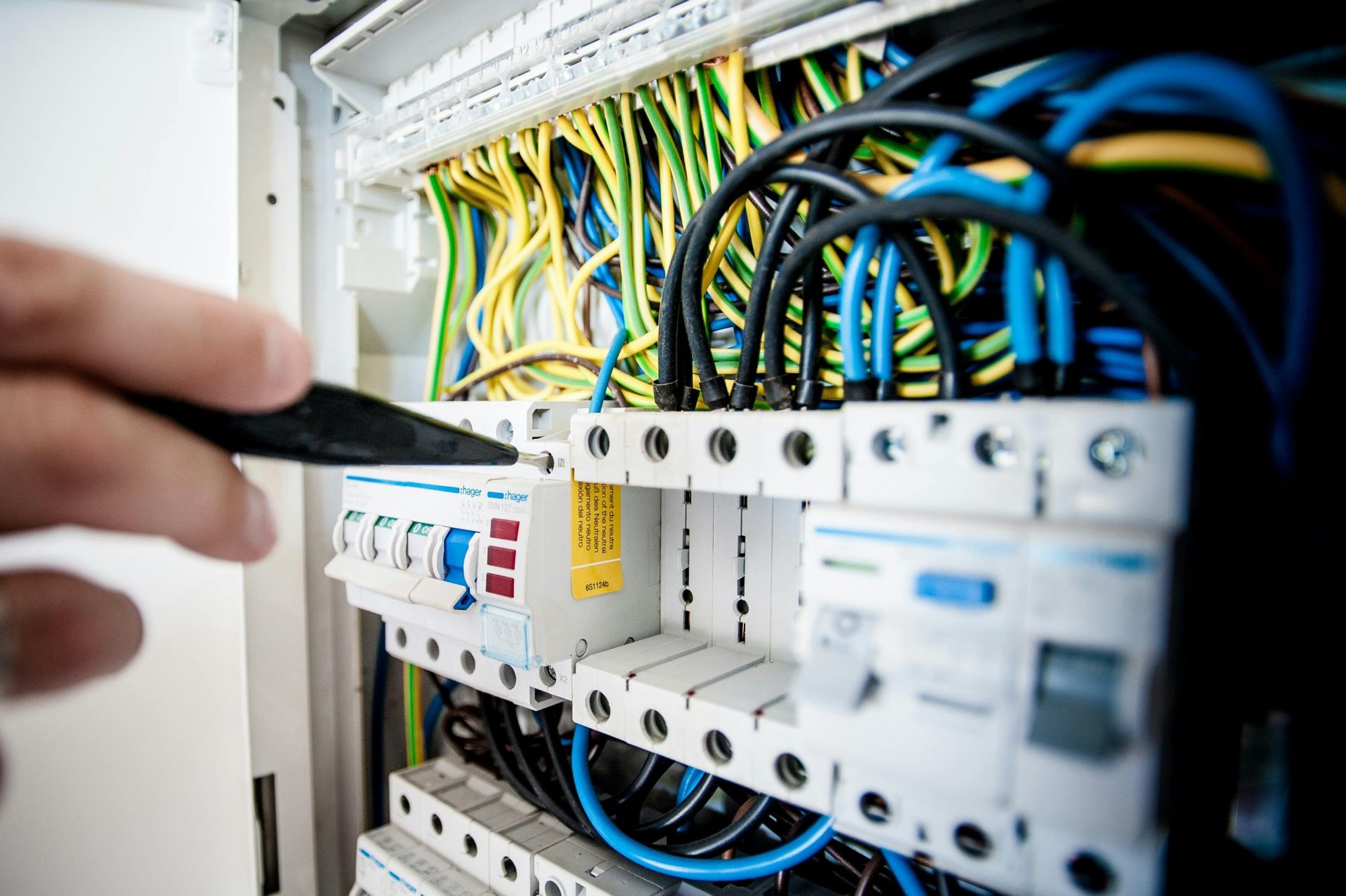Mano de un electricista trabajando en un panel de disyuntores con cables de colores, asegurando conexiones eléctricas seguras.