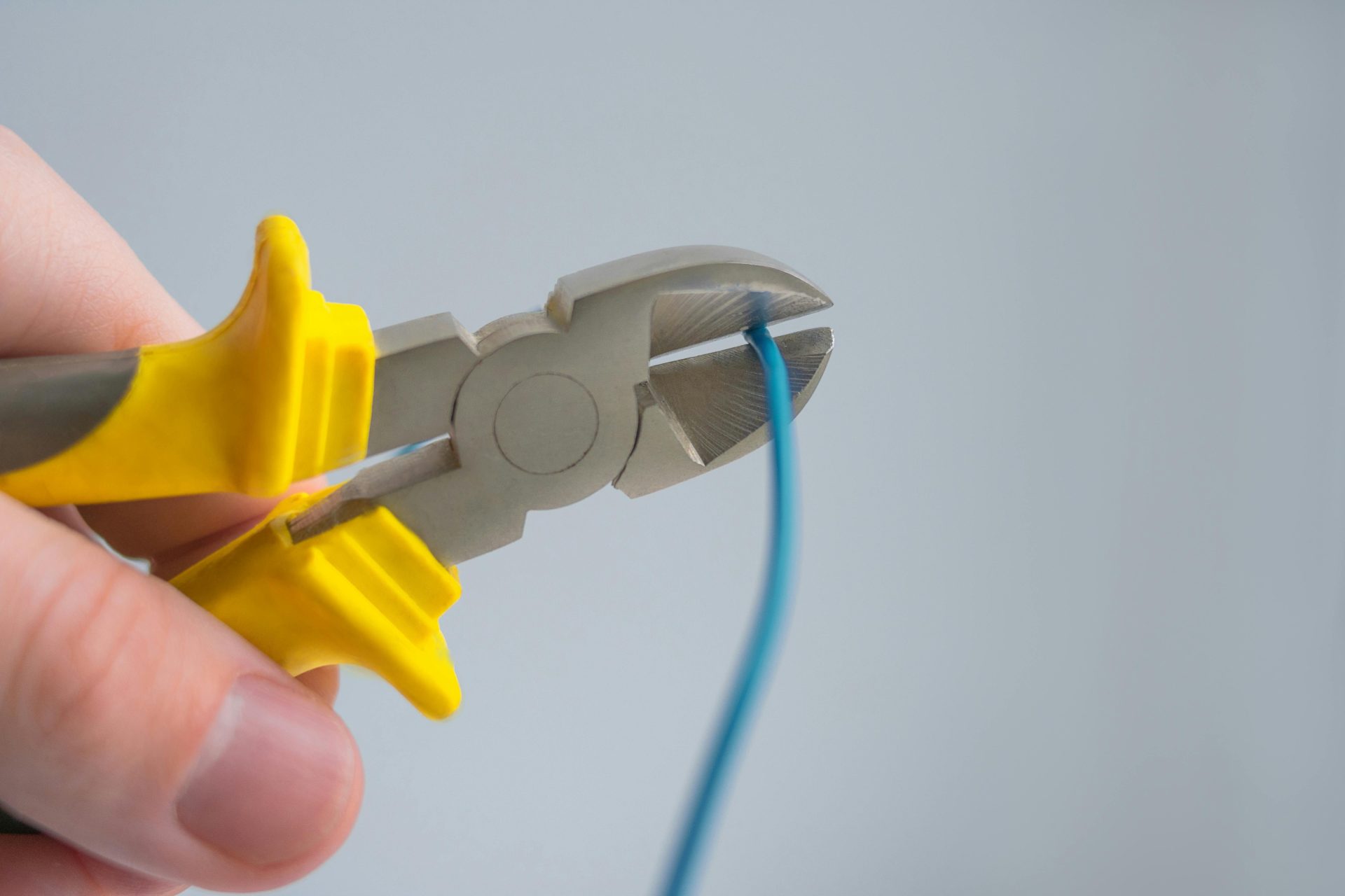Imagen detallada de una mano utilizando unos alicates con mango amarillo para cortar un cable azul.